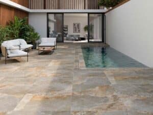 Terraza con piscina y suelo porcelánico antideslizante en tonos naturales, con mobiliario exterior blanco y verde.