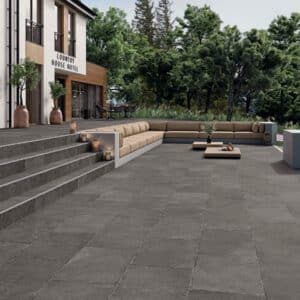 Amplia terraza de hotel rural con suelo porcelánico en gris oscuro, escaleras y muebles de exterior, rodeada de naturaleza.