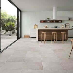 Cocina moderna con isla central y suelo porcelánico en tono gris claro, grandes ventanales que conectan con el jardín.