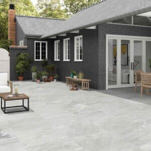 Patio con suelo porcelánico antideslizante gris, muebles de madera y fachada de casa moderna.
