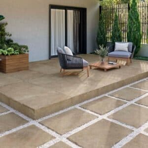 Terraza moderna con baldosas porcelánicas beige y mobiliario de exterior, rodeada de vegetación y diseño minimalista.