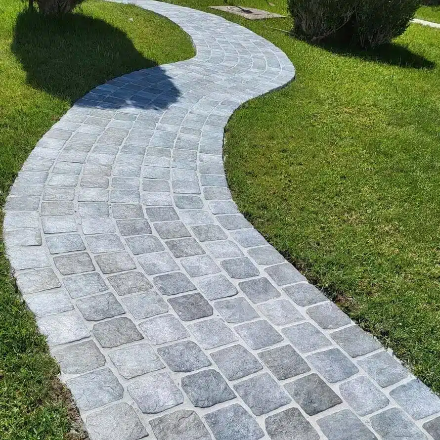Camino serpenteante hecho con baldosas de hormigón imitación piedra sobre un lecho de grava blanca.